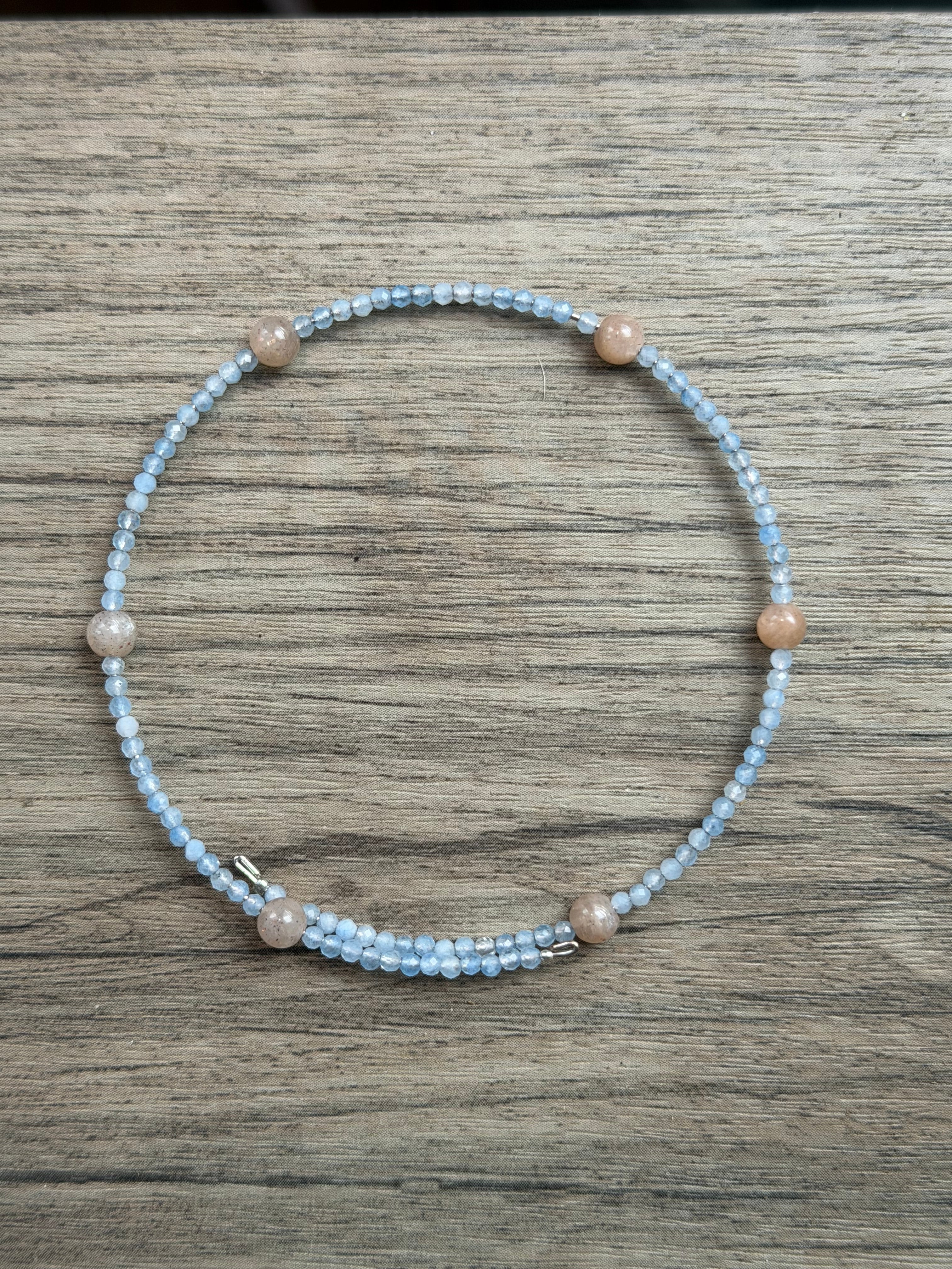 Beaded 2mm faceted aquamarine bracelet with smooth round sunstone beads on a wooden surface